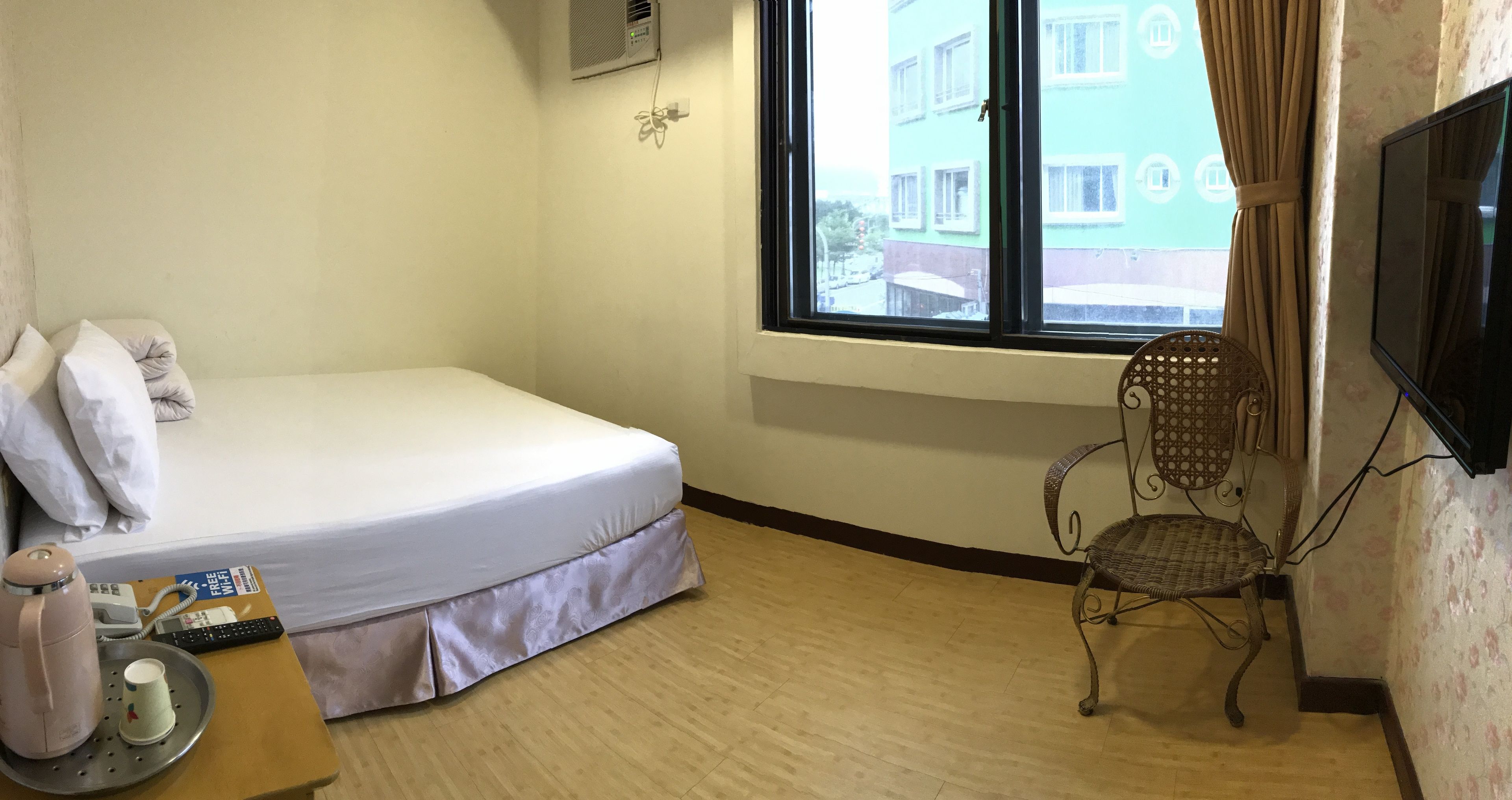 A hotel room with a bed, a chair, a TV, and a window with a view of buildings.