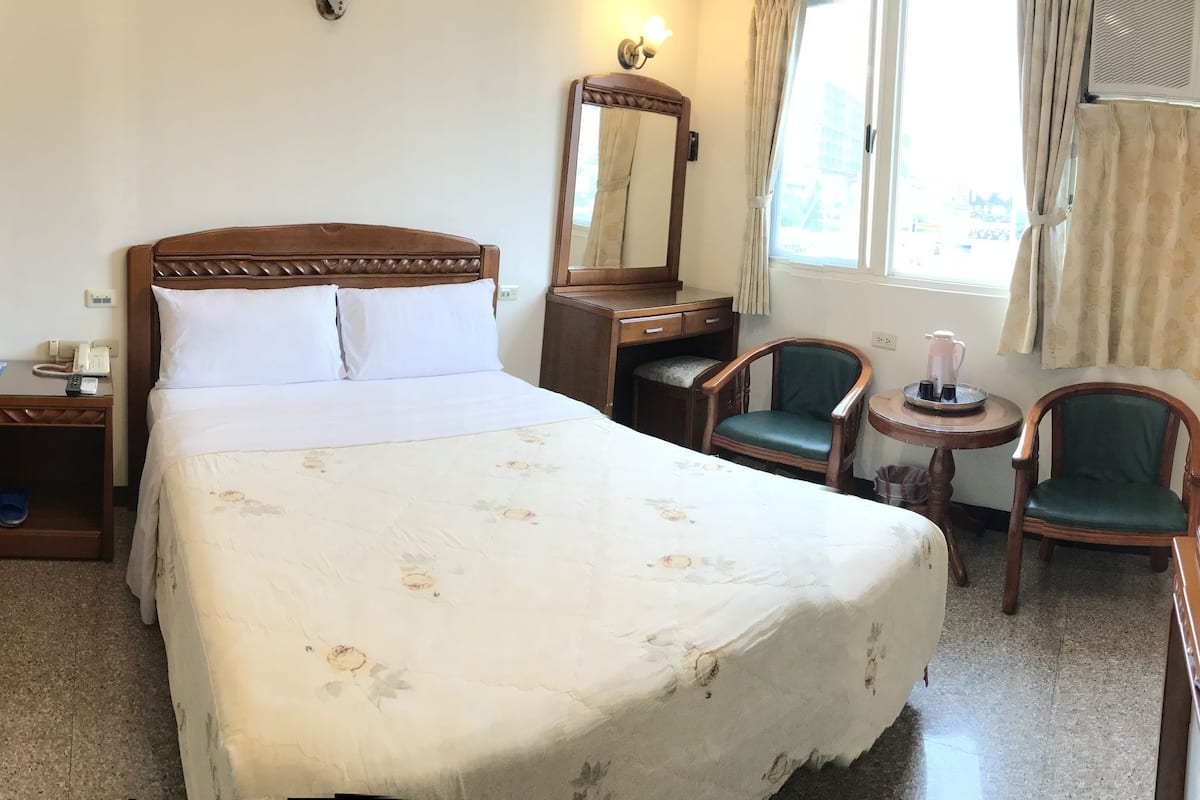 A hotel room with a bed, a desk with a computer, a chair, a TV, and a window with curtains.