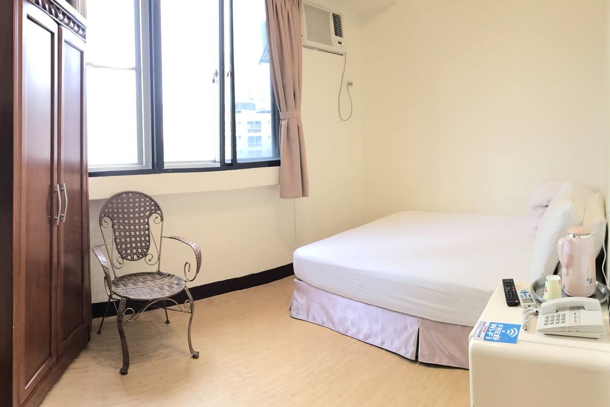 A hotel room with a bed, a chair, a desk with a phone, a TV, and a window with curtains.