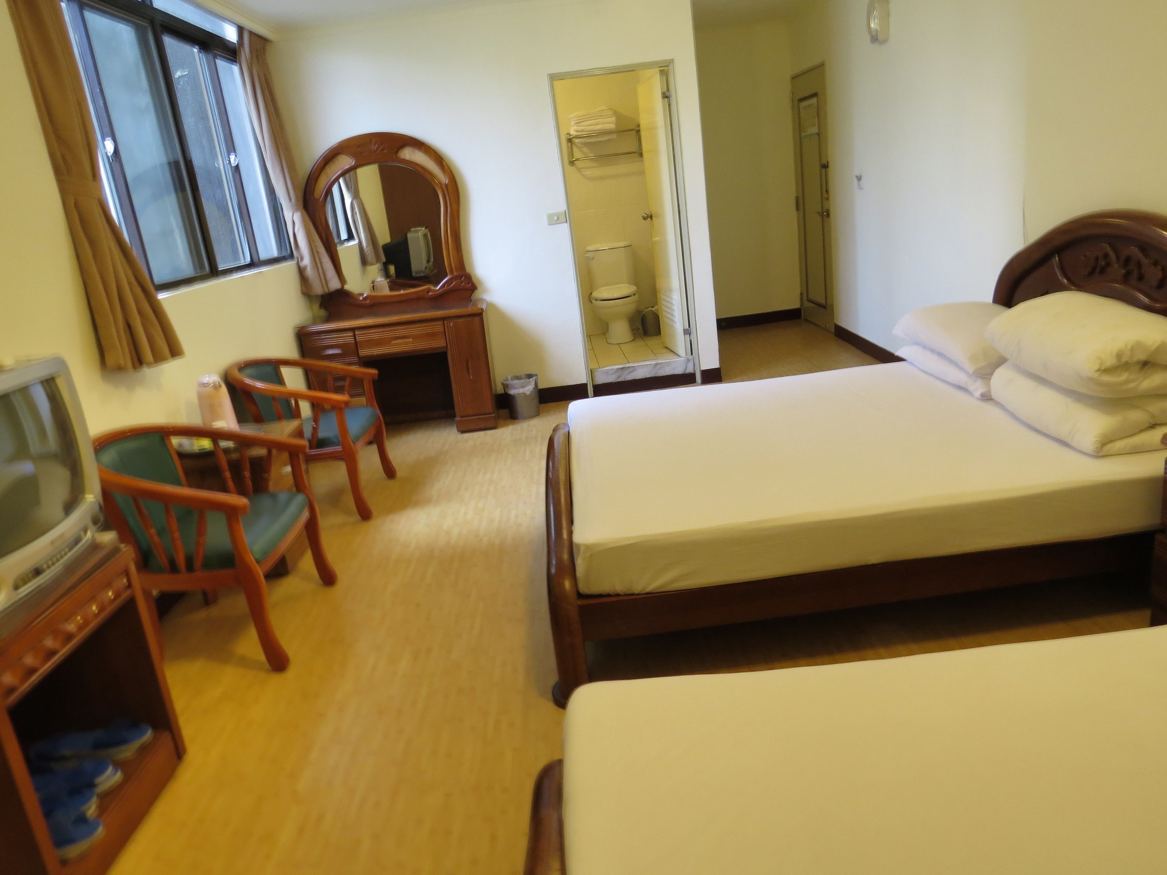 A hotel room with a bed, a desk, a chair, a television, and a mirror.