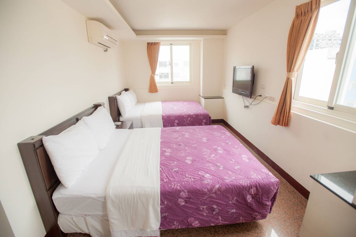 A hotel room with two beds, a TV, and a window with curtains.