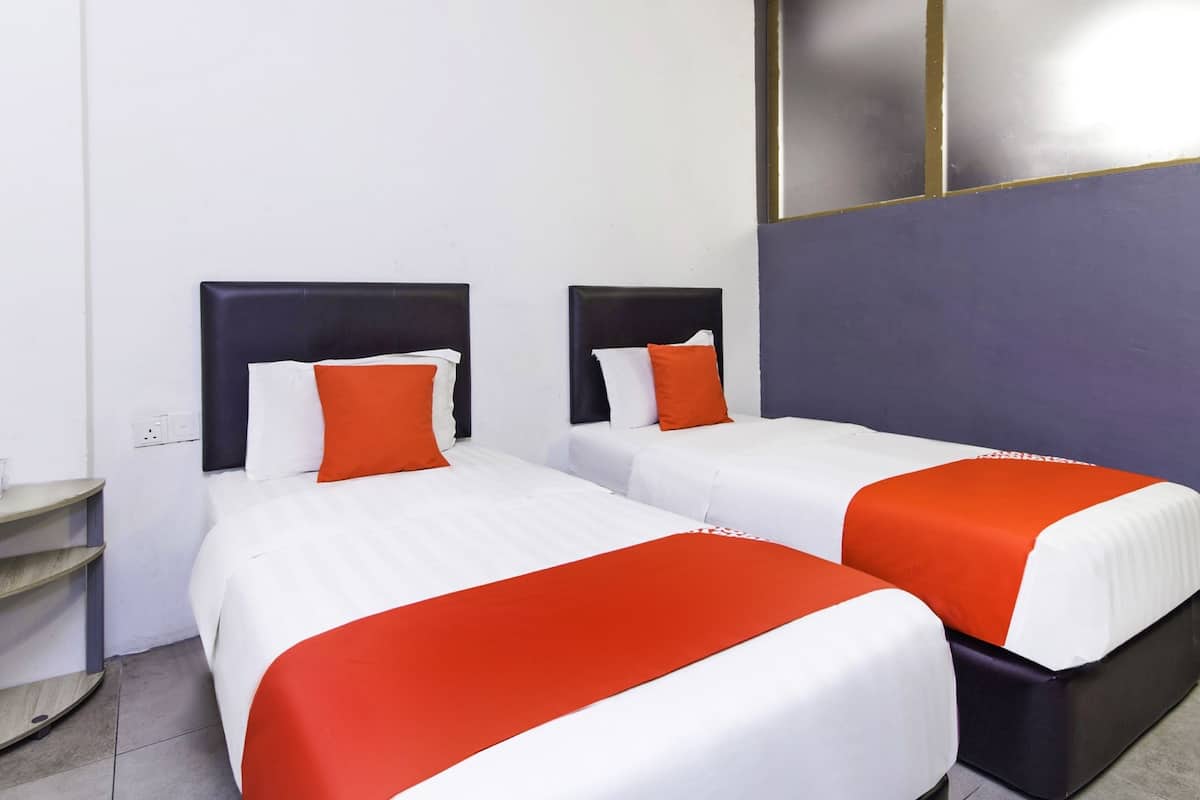 A hotel room with two beds, each with a white and orange bedspread, and a dark headboard.