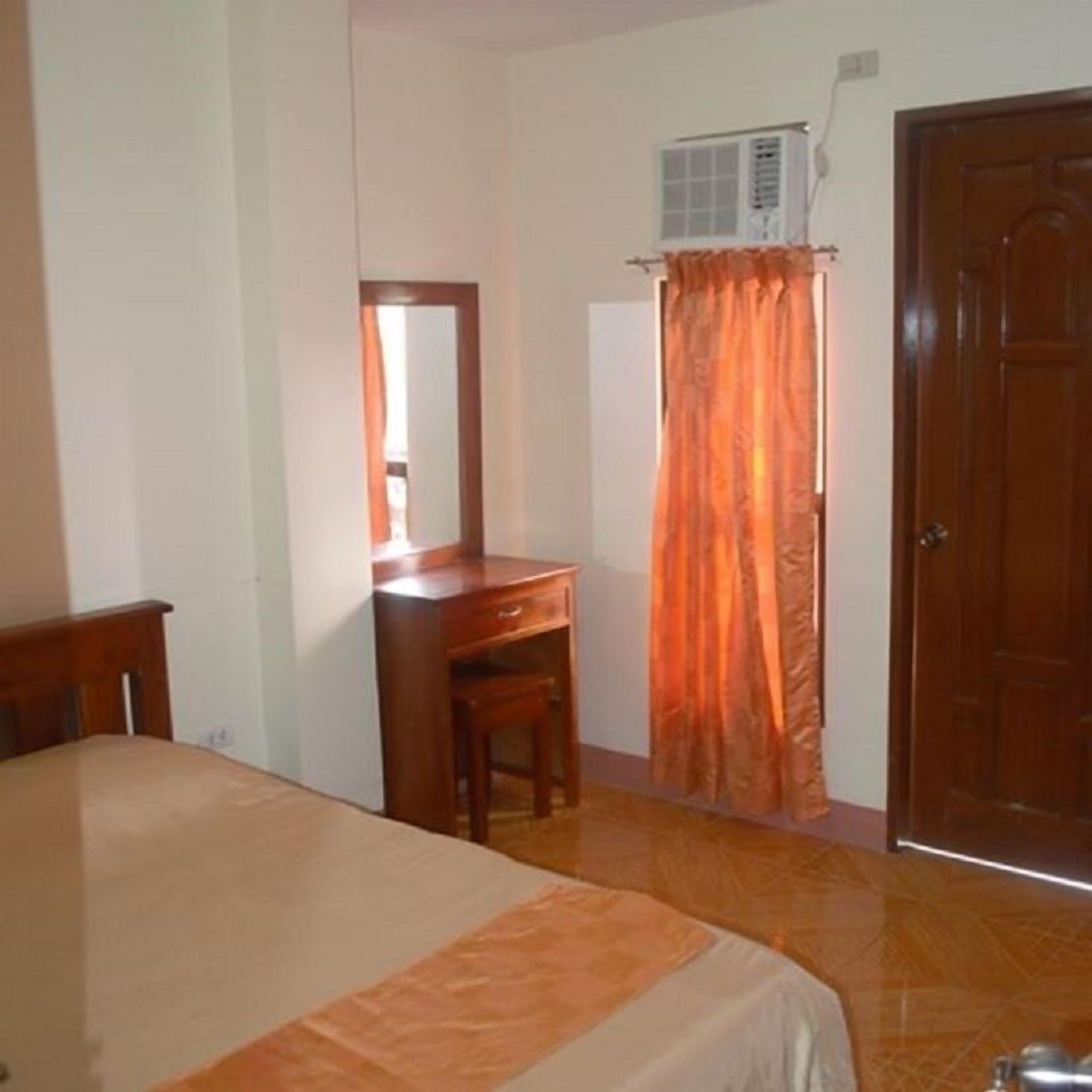 Un dormitorio con cama, escritorio de madera, espejo, equipo de aire acondicionado y una puerta.