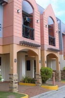 Un edificio de varios pisos con fachada rosa, pilares de piedra y un balcón con barandilla de metal.