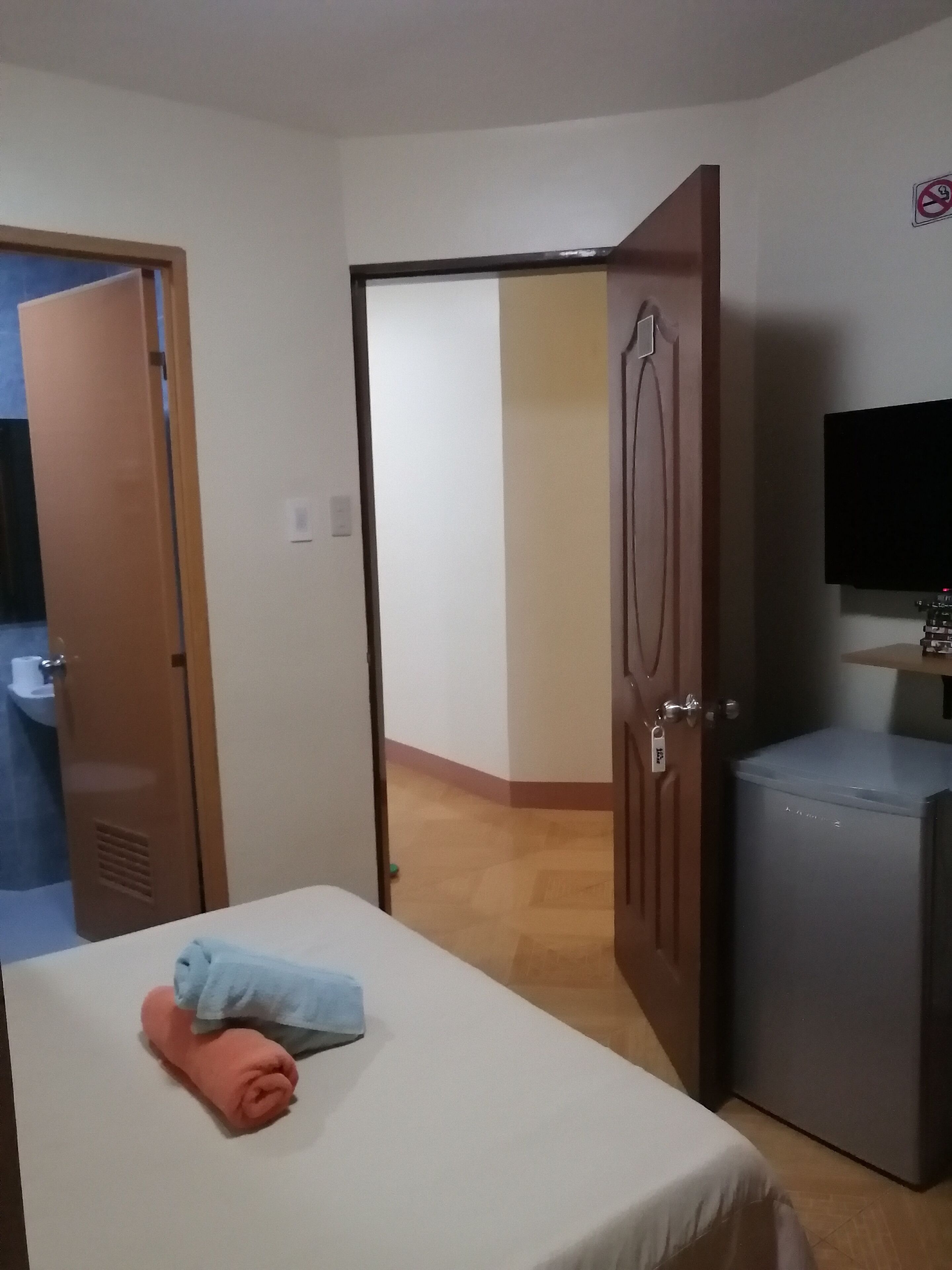 Habitación de hotel con cama, refrigerador pequeño, televisión y baño visible a través de una puerta abierta.