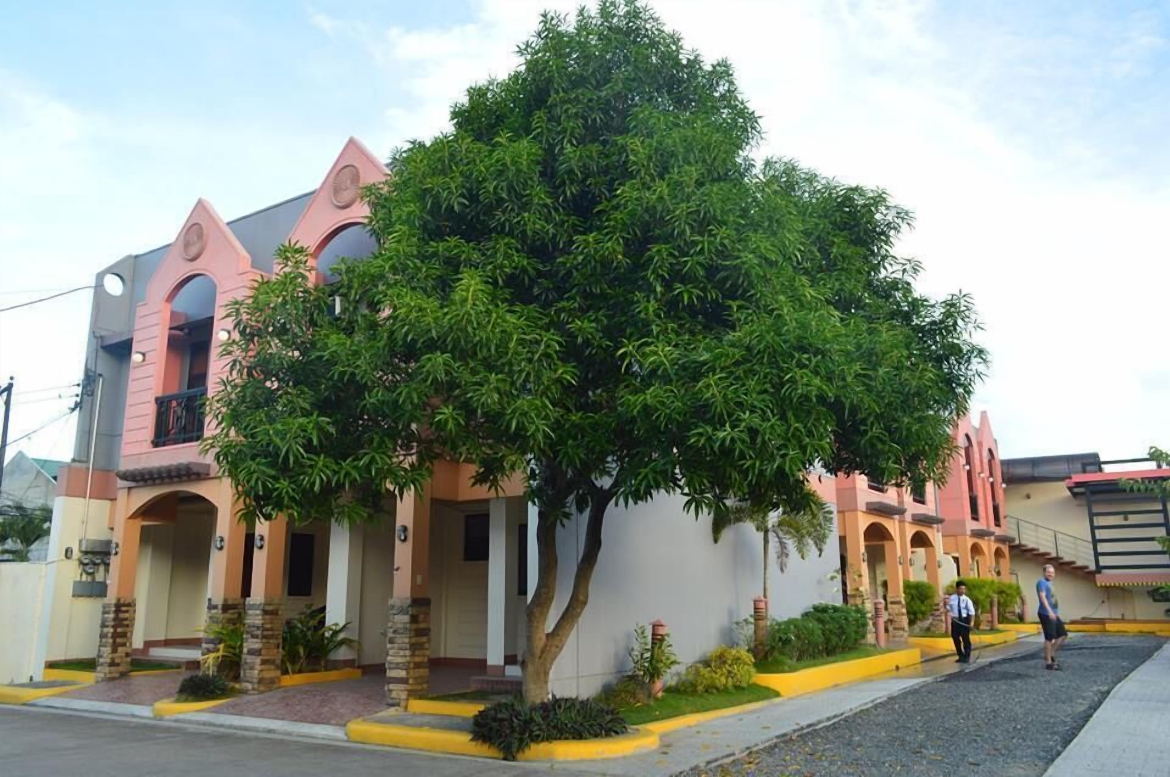 A building with a pink facade, arched windows, and a large tree in front.