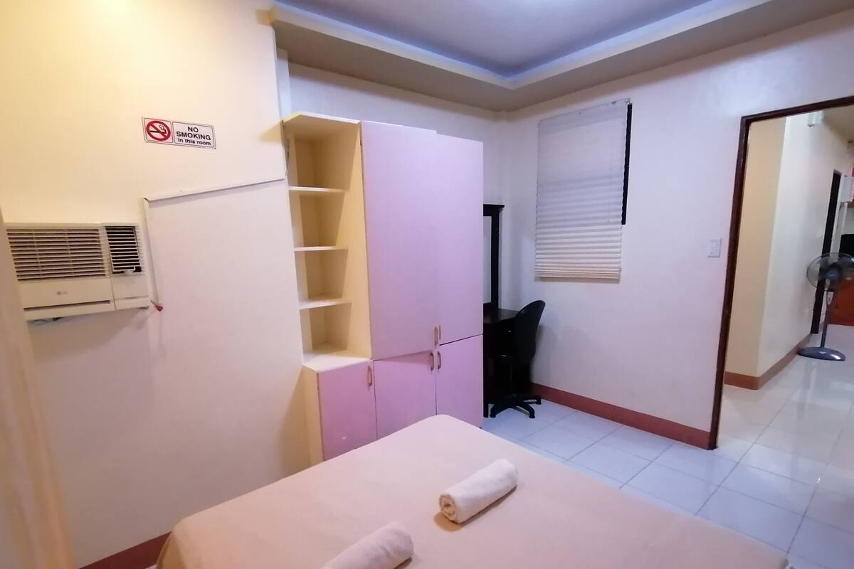Quarto com cama, guarda-roupa, escrivaninha e cadeira. Sinal de proibido fumar na parede.