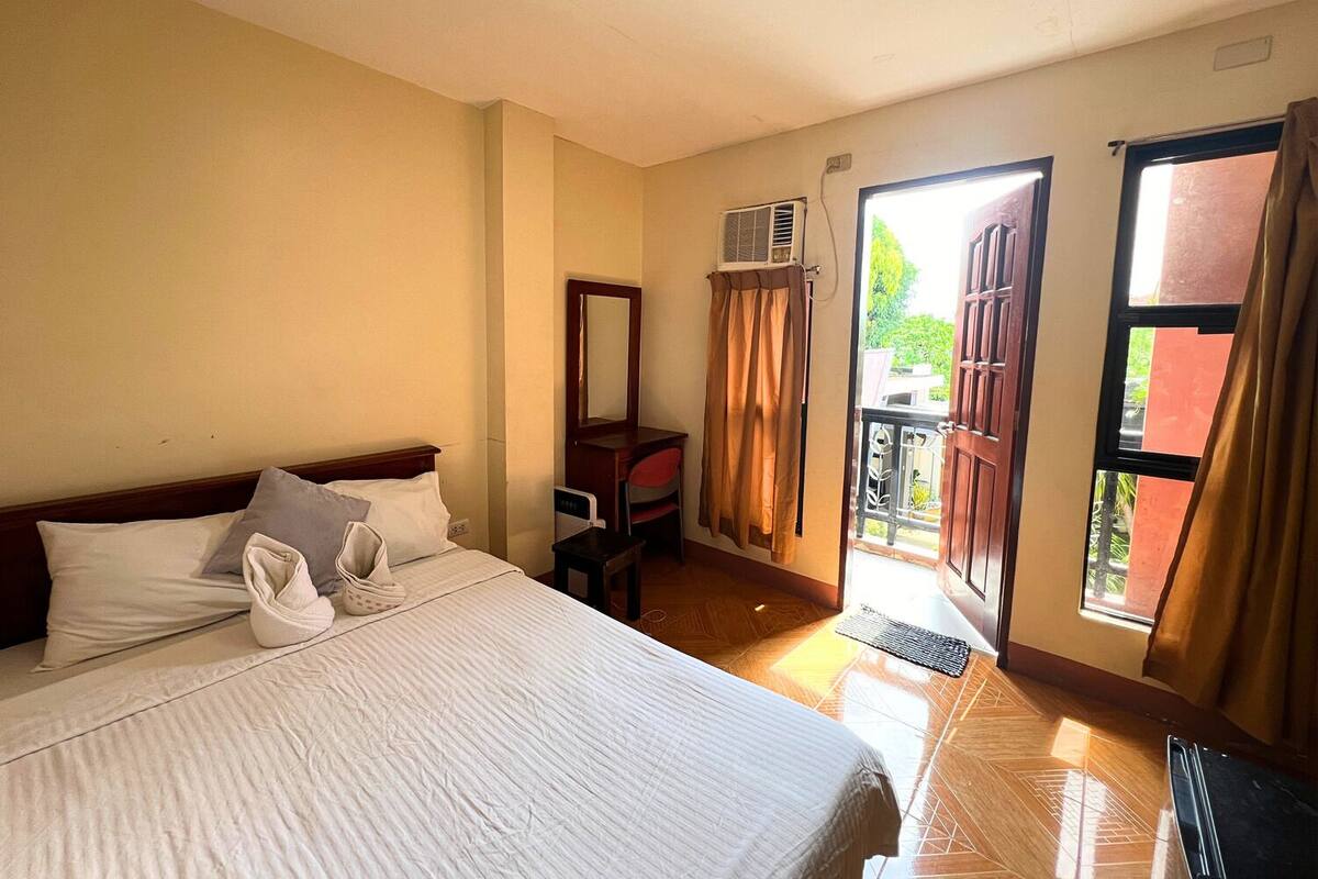 Quarto de hotel com cama, escrivaninha, ar condicionado e vista para o exterior.