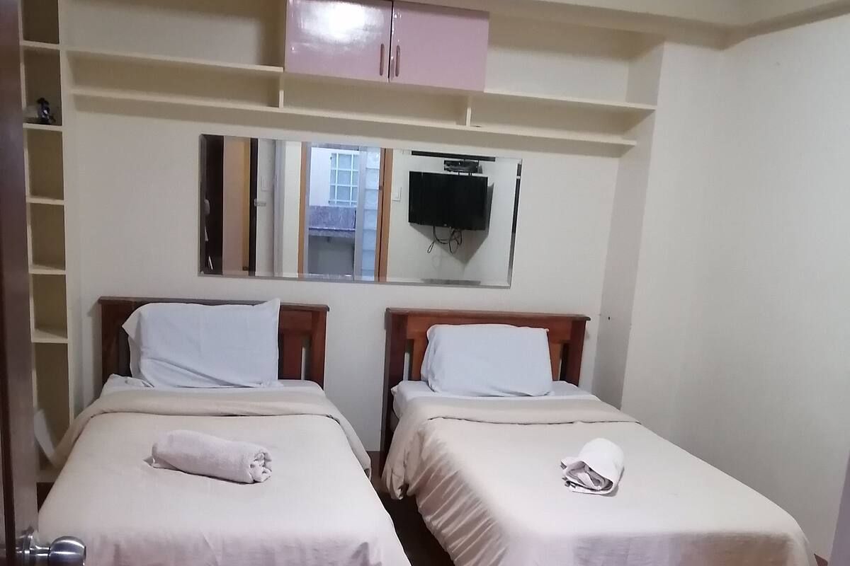 Quarto com duas camas, televisão e espelho.