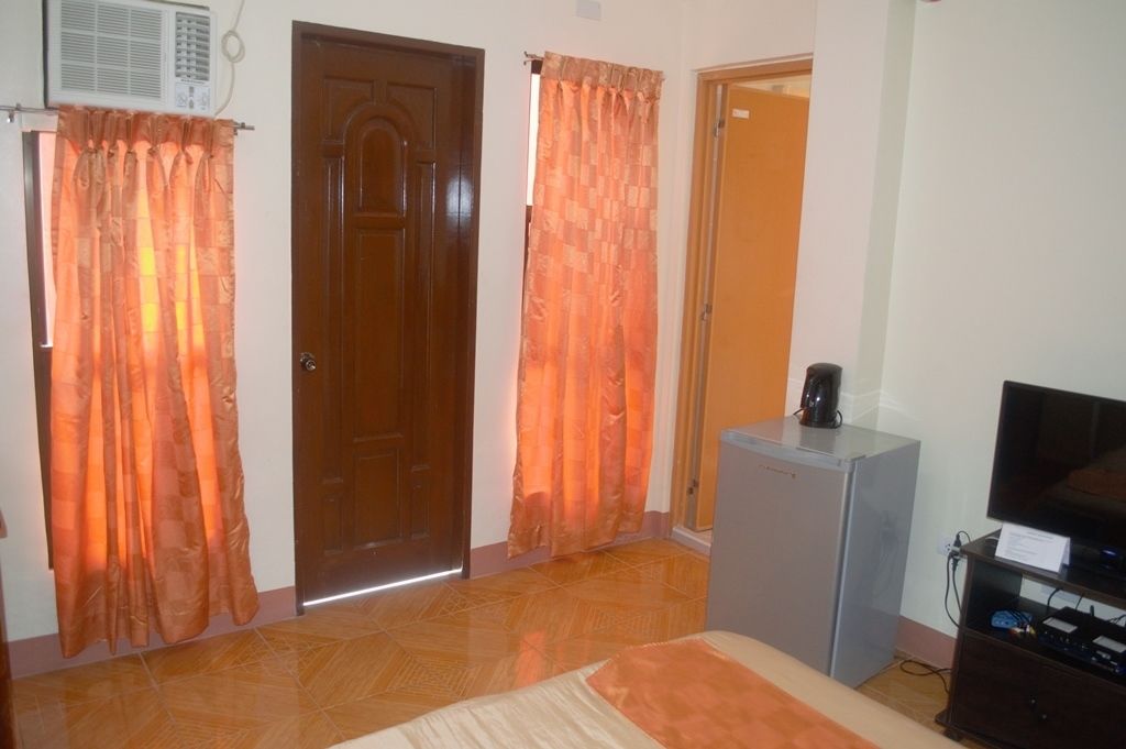 Quarto com duas portas, uma televisão sobre um móvel e um frigorífico.