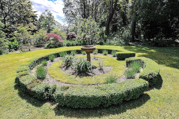 A meticulously landscaped garden with a central circular hedge, a birdbath, and various shrubs.