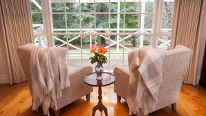 A room with two upholstered chairs, a small round table, and a vase with flowers. - Moulton Park Homestead (Sassafras)