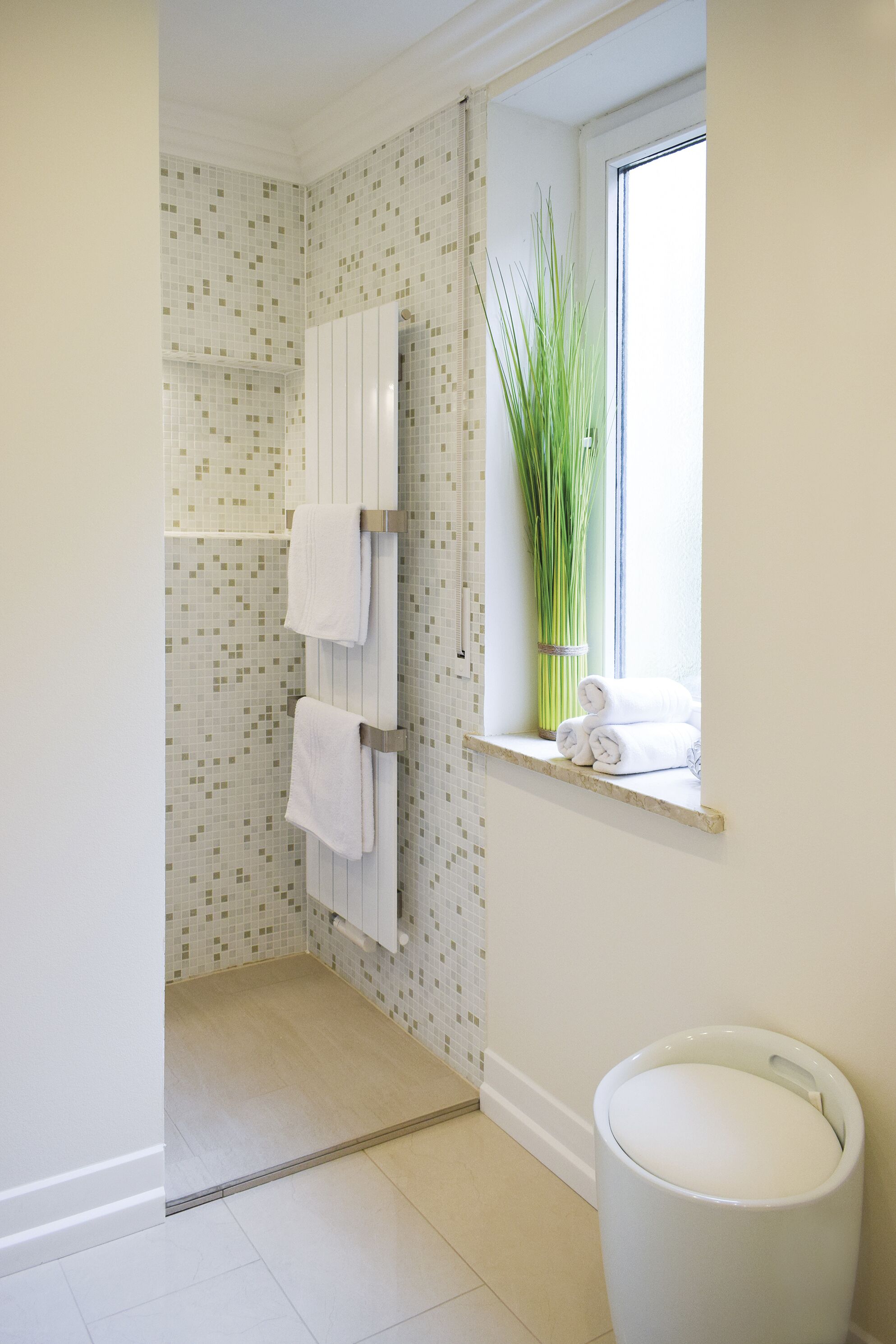 A bathroom with a tiled floor, a window with a plant, and a towel rack with towels.