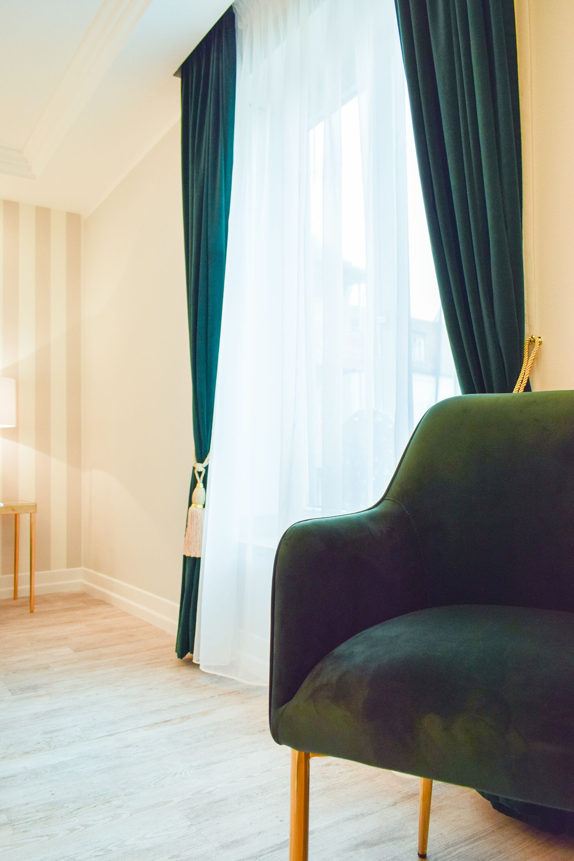 A room with a green sofa, a lamp, and sheer curtains.