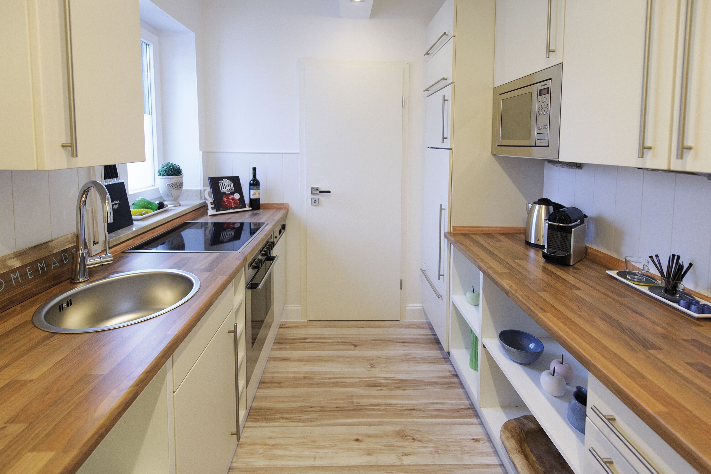A modern kitchen with a stainless steel sink, wooden countertops, a built-in oven, and white cabinetry.