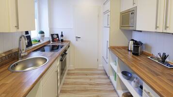 A modern kitchen with a stainless steel sink, wooden countertops, a built-in oven, and white cabinetry.