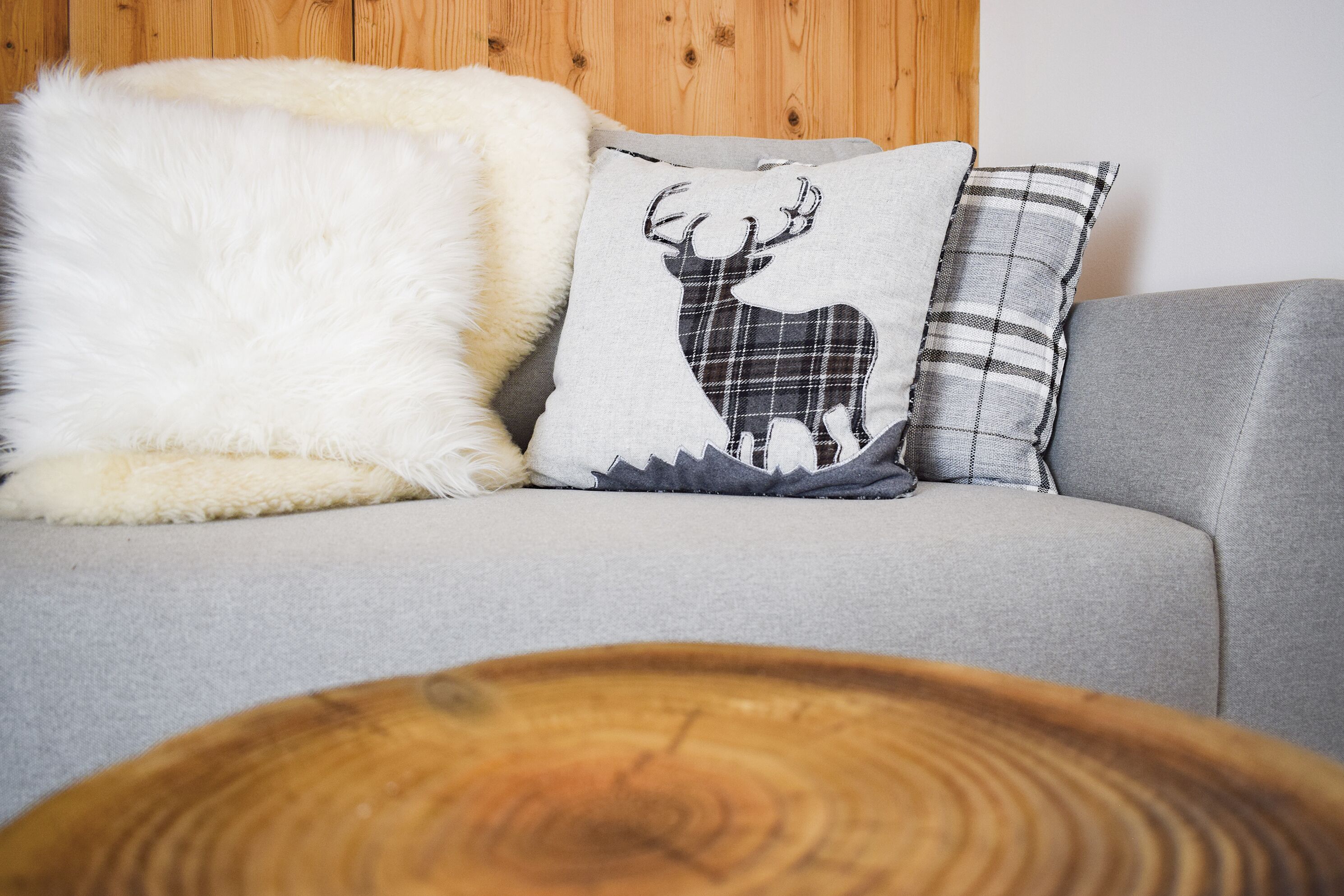 Un sofá gris con tres almohadones decorativos, uno con un diseño de ciervo, y una mesa redonda de madera al frente.