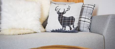A grey sofa with three decorative pillows, one featuring a deer design, and a round wooden table in the foreground.