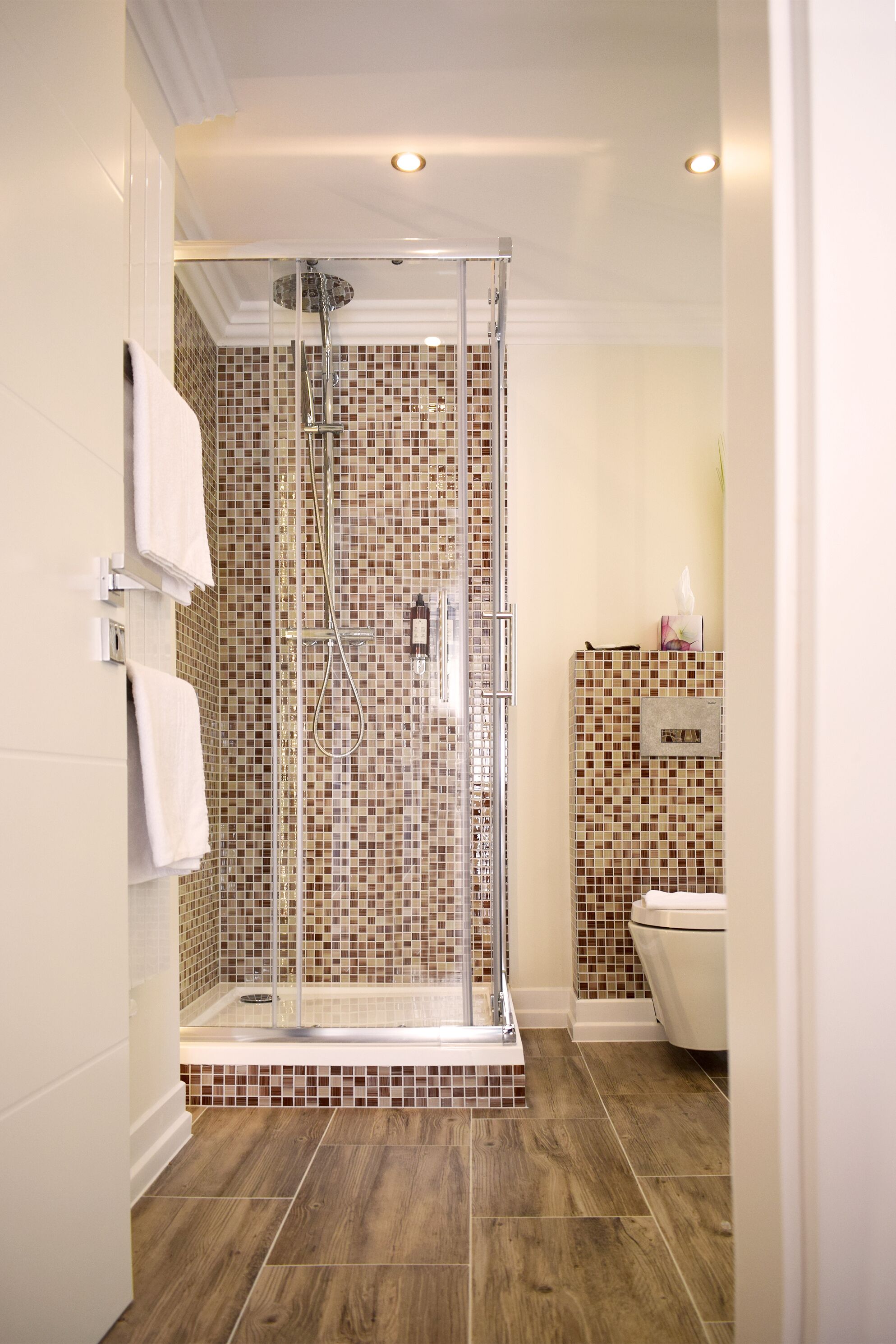 A modern bathroom with a glass-enclosed shower, tiled walls, and a wooden floor.