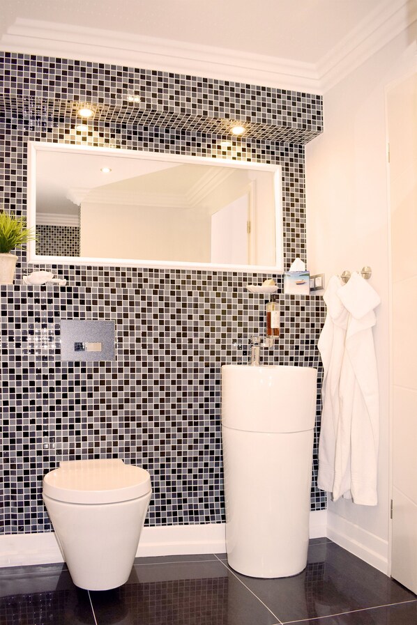 Un baño con pared de mosaicos blanco y negro, un lavamanos blanco y un inodoro.