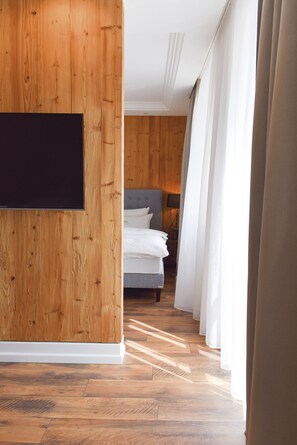 A hotel room with wooden paneling, a flat-screen TV mounted on the wall, a bed with white bedding, and a window with sheer curtains. - Donau Lodge Boardinghouse (Straubing)