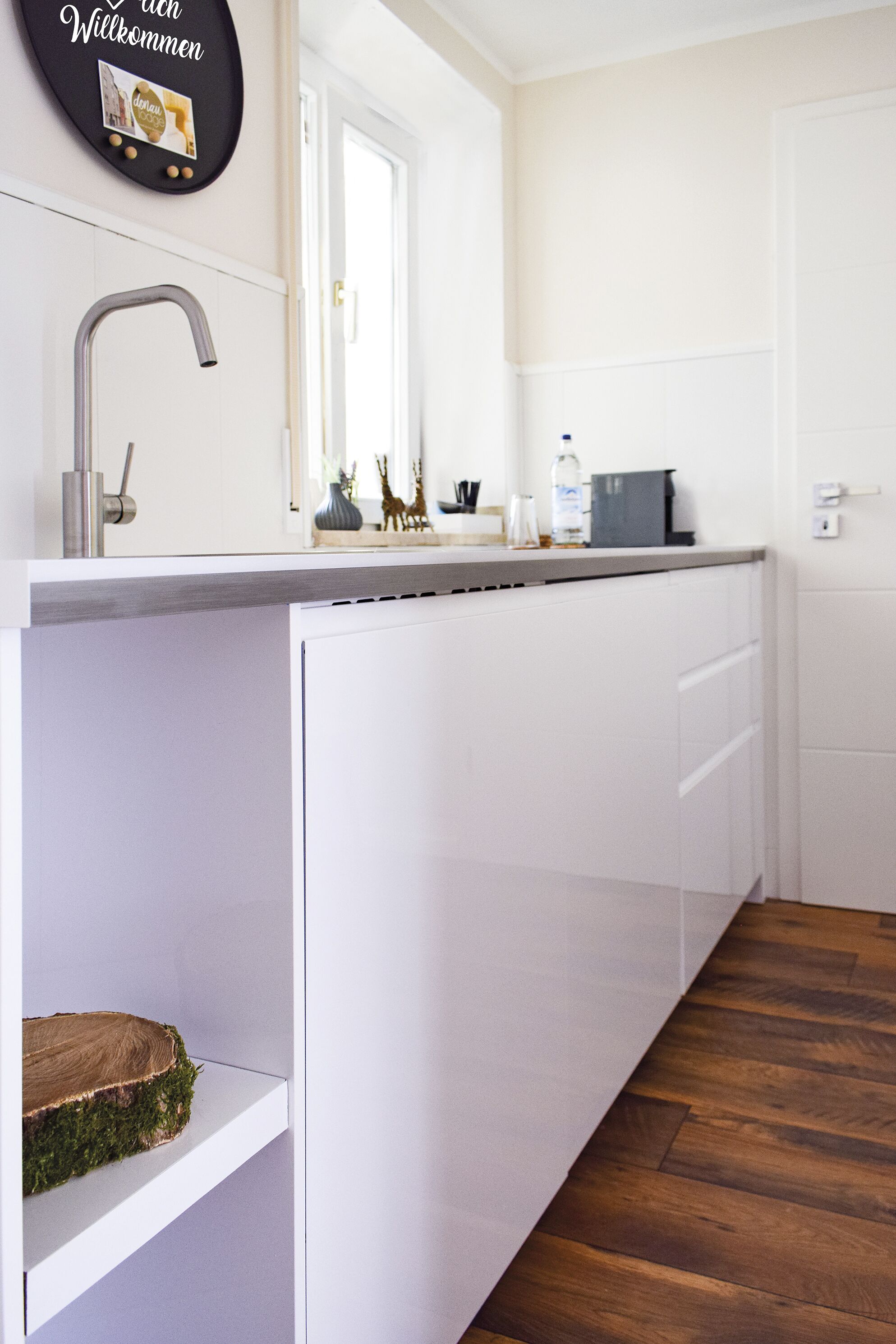 Una cocina moderna con un lavamanos empotrado, armarios blancos y suelo de madera.