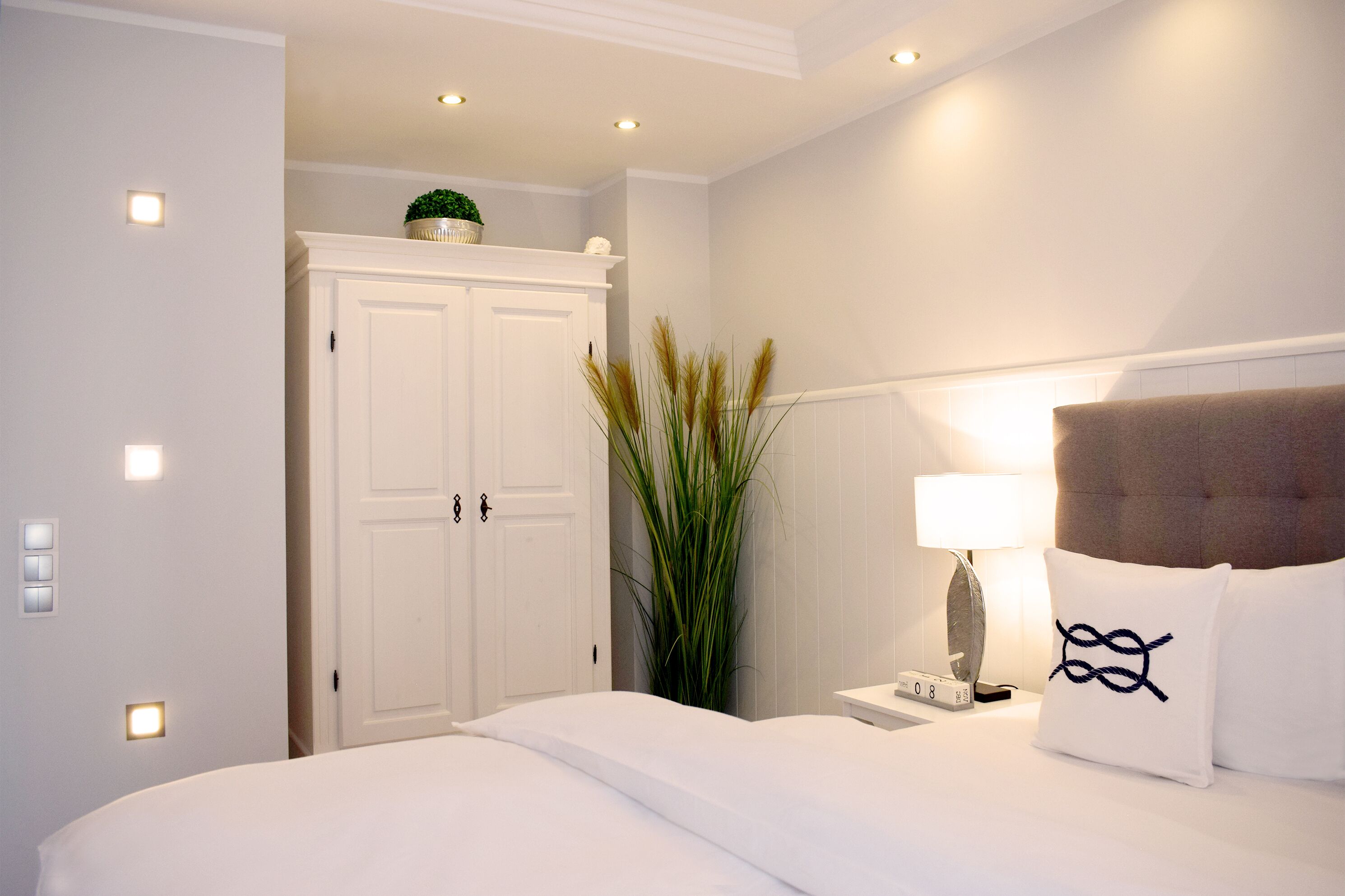 Ein Hotelzimmer mit Bett, Nachttisch, Lampe, Pflanze und Kleiderschrank.