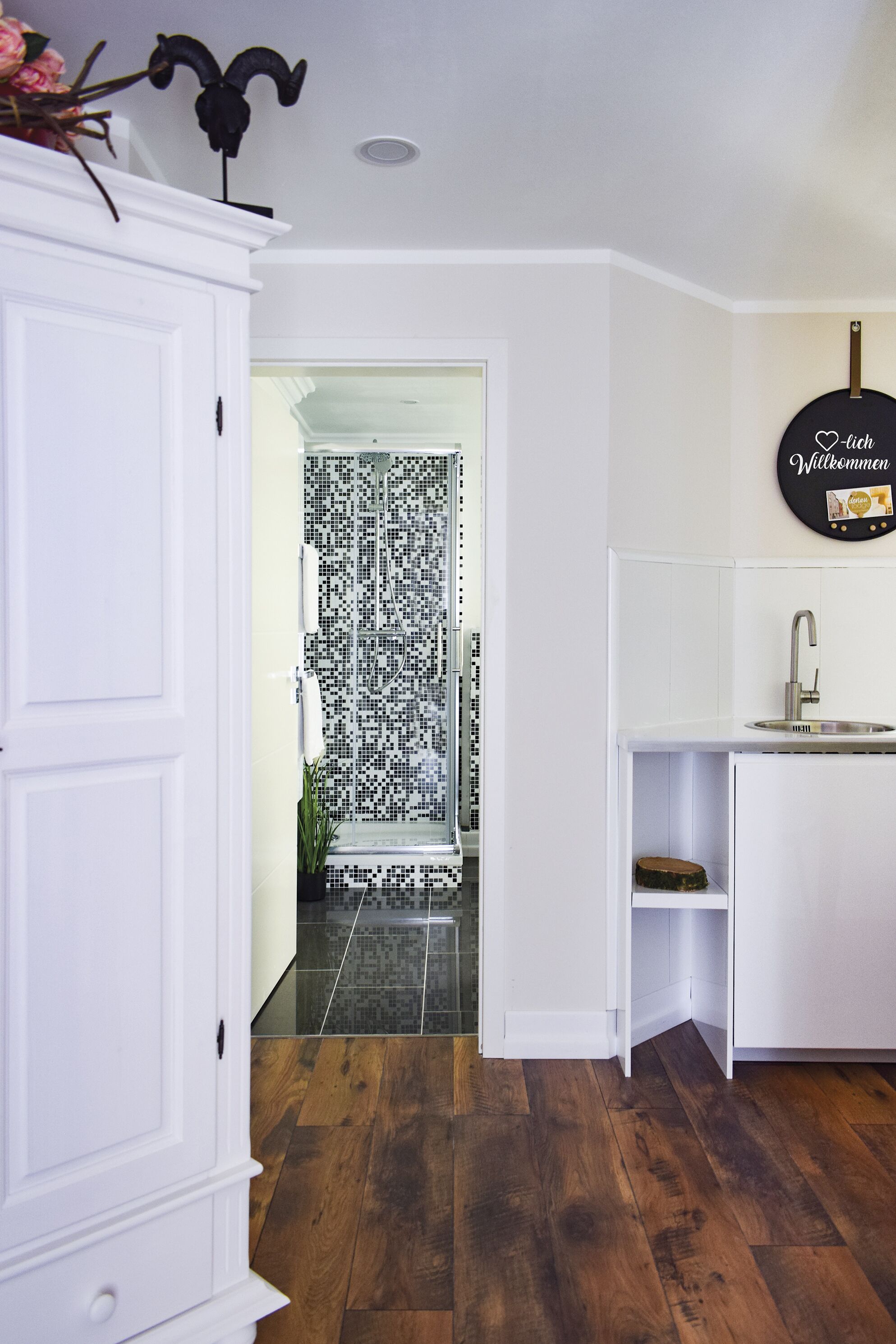 A modern kitchen with white cabinetry, a black and white tiled backsplash, and a wooden floor.