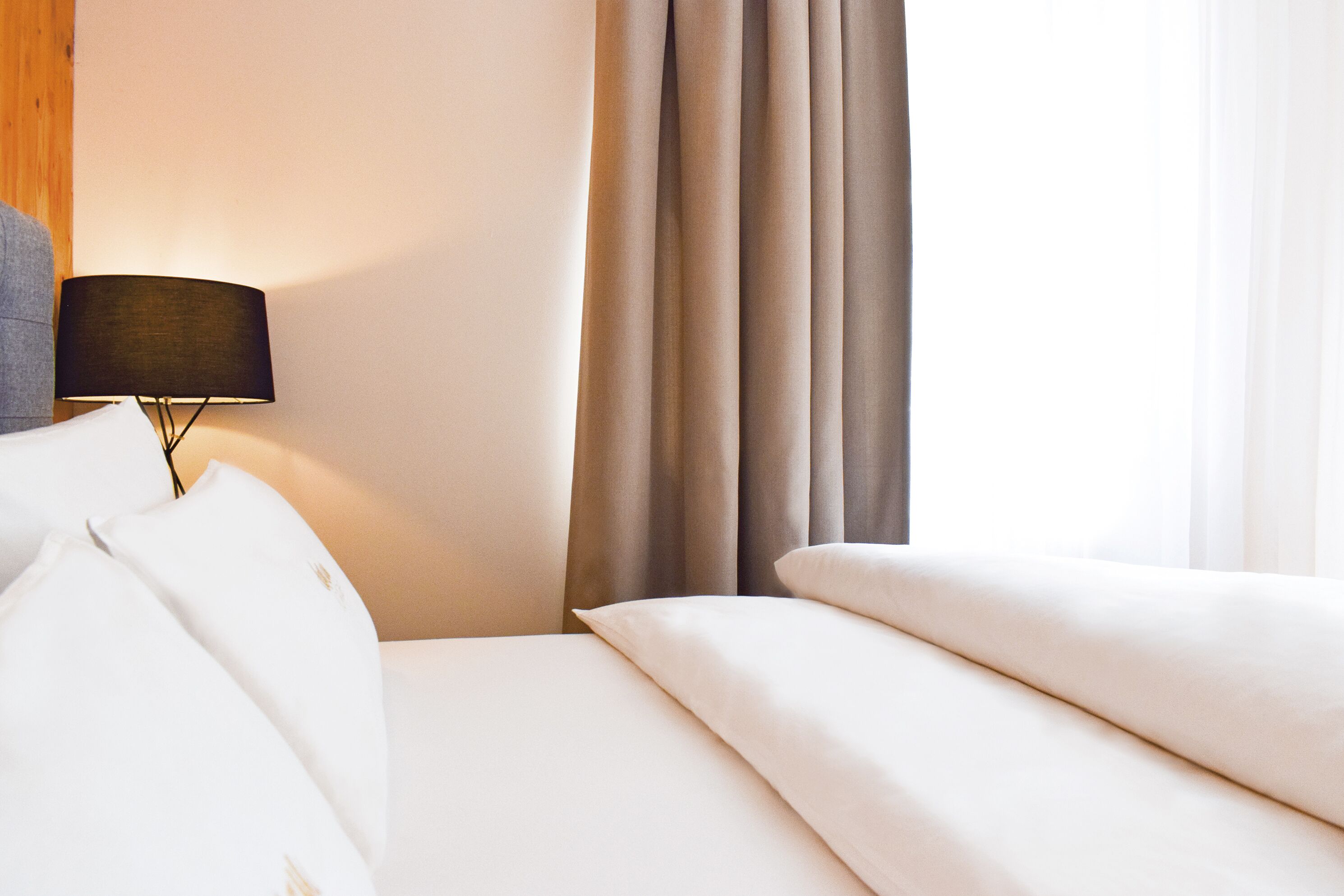 A hotel room with a bed, a lamp, and curtains.