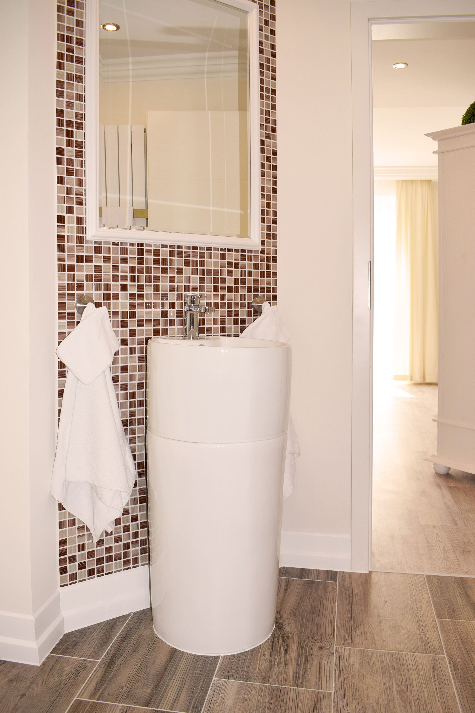 Une salle de bain avec un lavabo blanc, un miroir et un mur recouvert de carreaux.