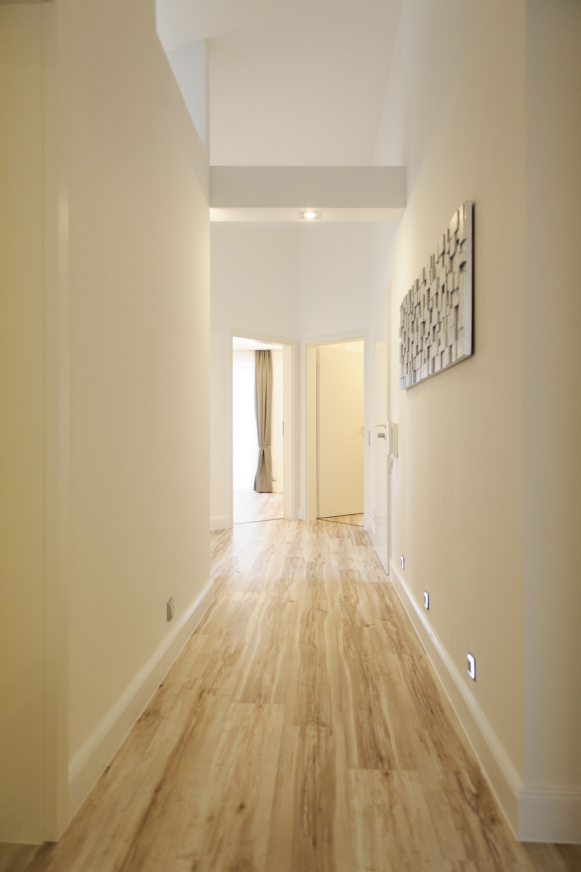 A hallway with wooden flooring, white walls, and a ceiling light.