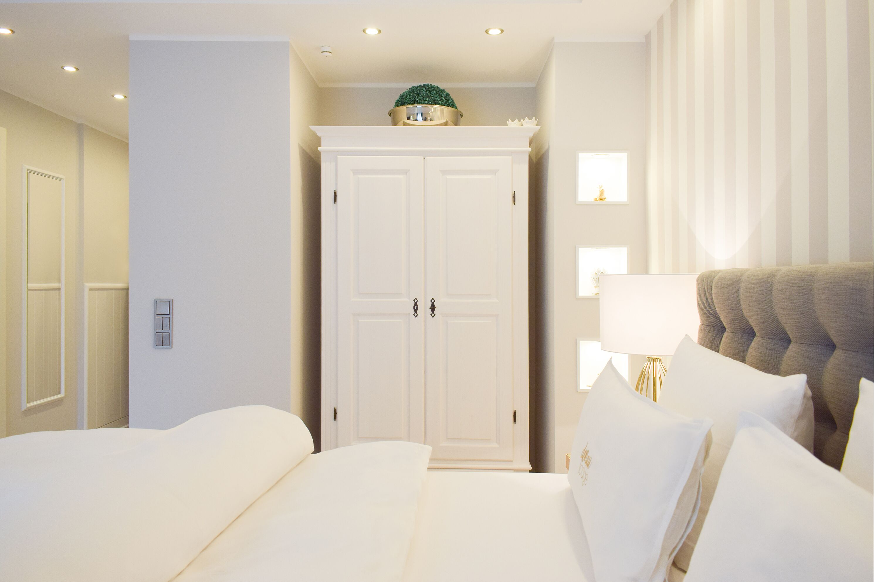 A hotel room with a large white wardrobe, a bed with white linens, and a bedside lamp.