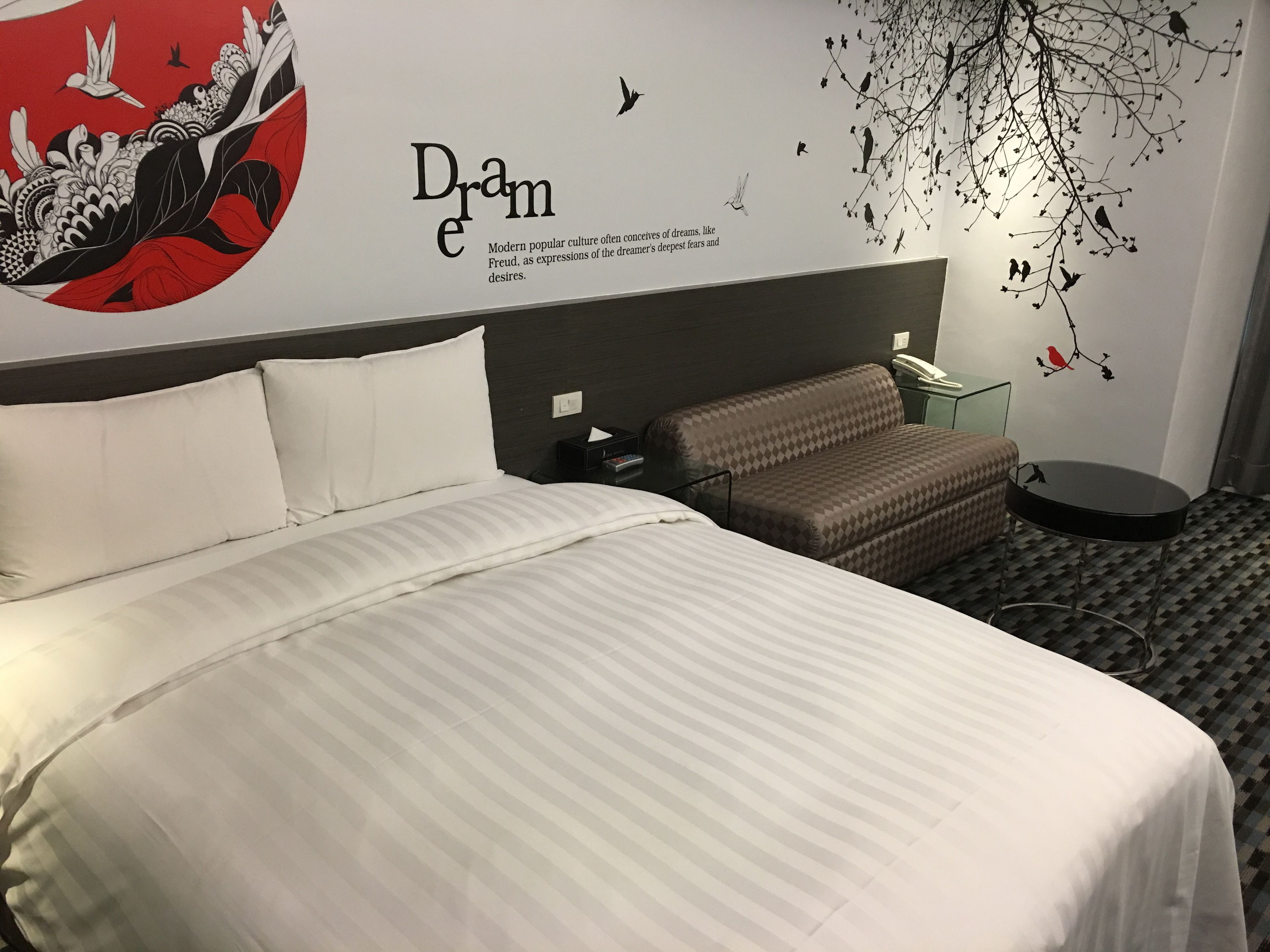 A hotel room with a large bed, a sofa, a small table, and a wall decoration.