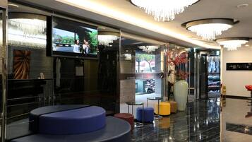 A modern lobby with a large TV screen, seating areas, and a chandelier.