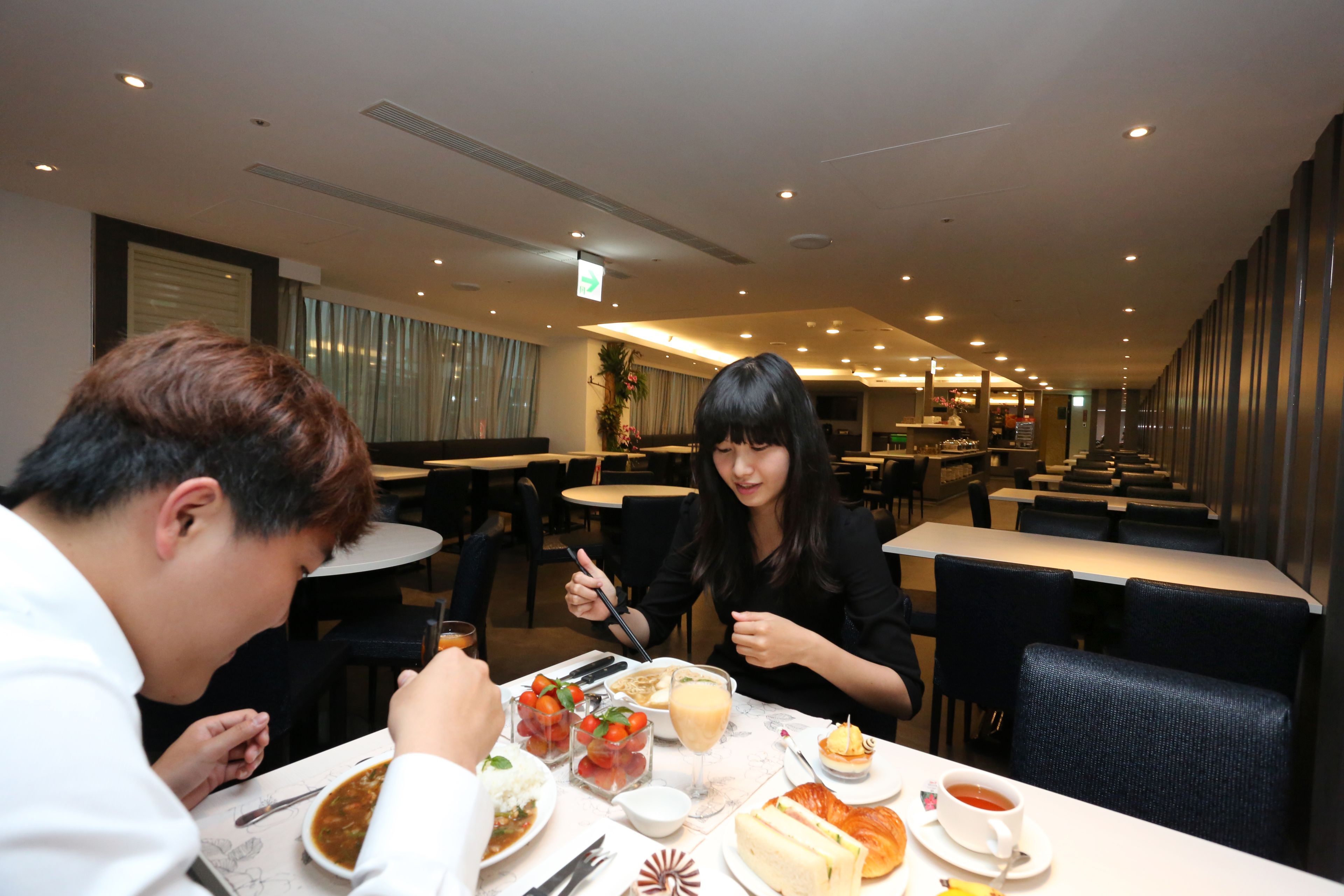 A dining area with tables and chairs, a buffet with various dishes, and a sign indicating the direction to the restrooms.