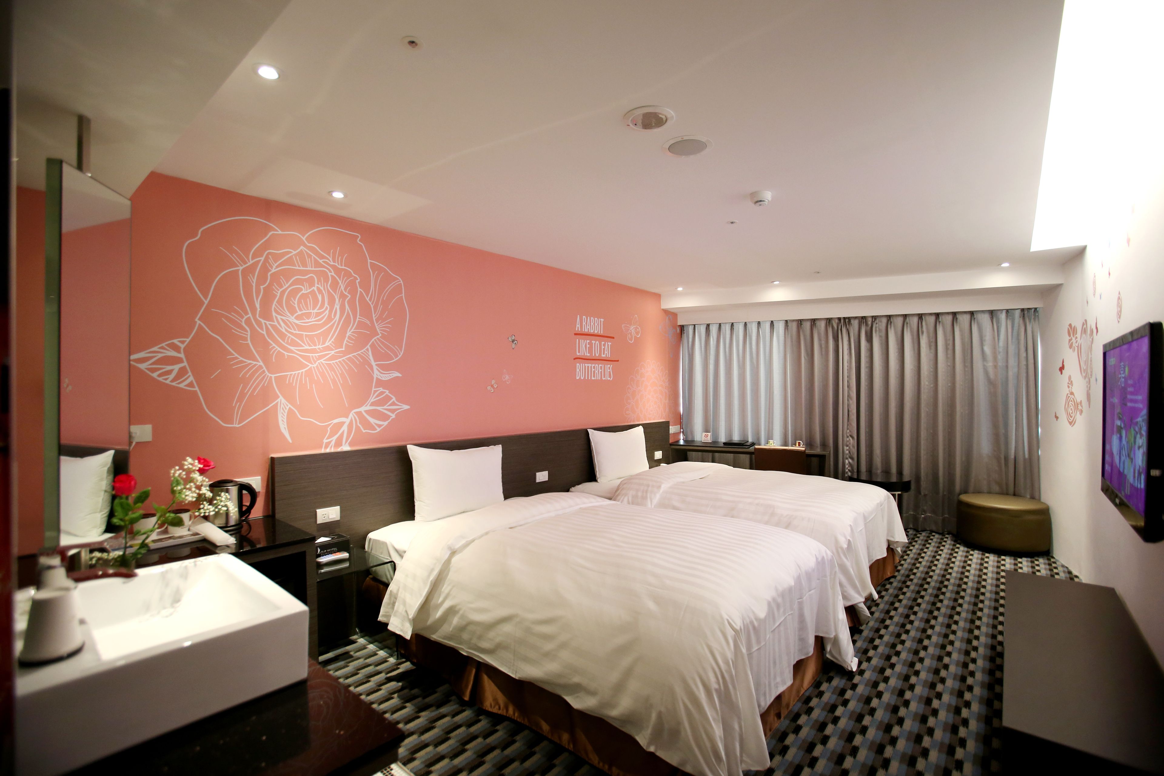 Habitación de hotel con dos camas, un mural grande en la pared, un baño con lavamanos y un televisor montado en la pared.