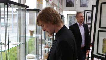 A person examining items on glass shelves in a room with framed pictures on the walls and a tiled floor.