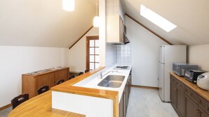 A compact kitchen with a central island, wooden cabinets, a built-in microwave, and a refrigerator. - The Heritage (Kutchan)
