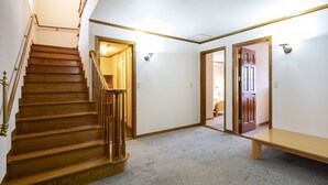 A hallway with a wooden staircase, a bench, and doors leading to other rooms. - The Heritage (Kutchan)