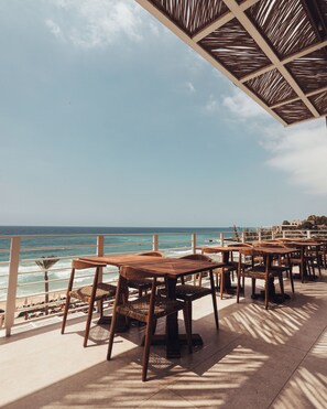 An outdoor seating area with wooden tables and chairs, overlooking the ocean. - Ocean Blue Resort (Mastita)