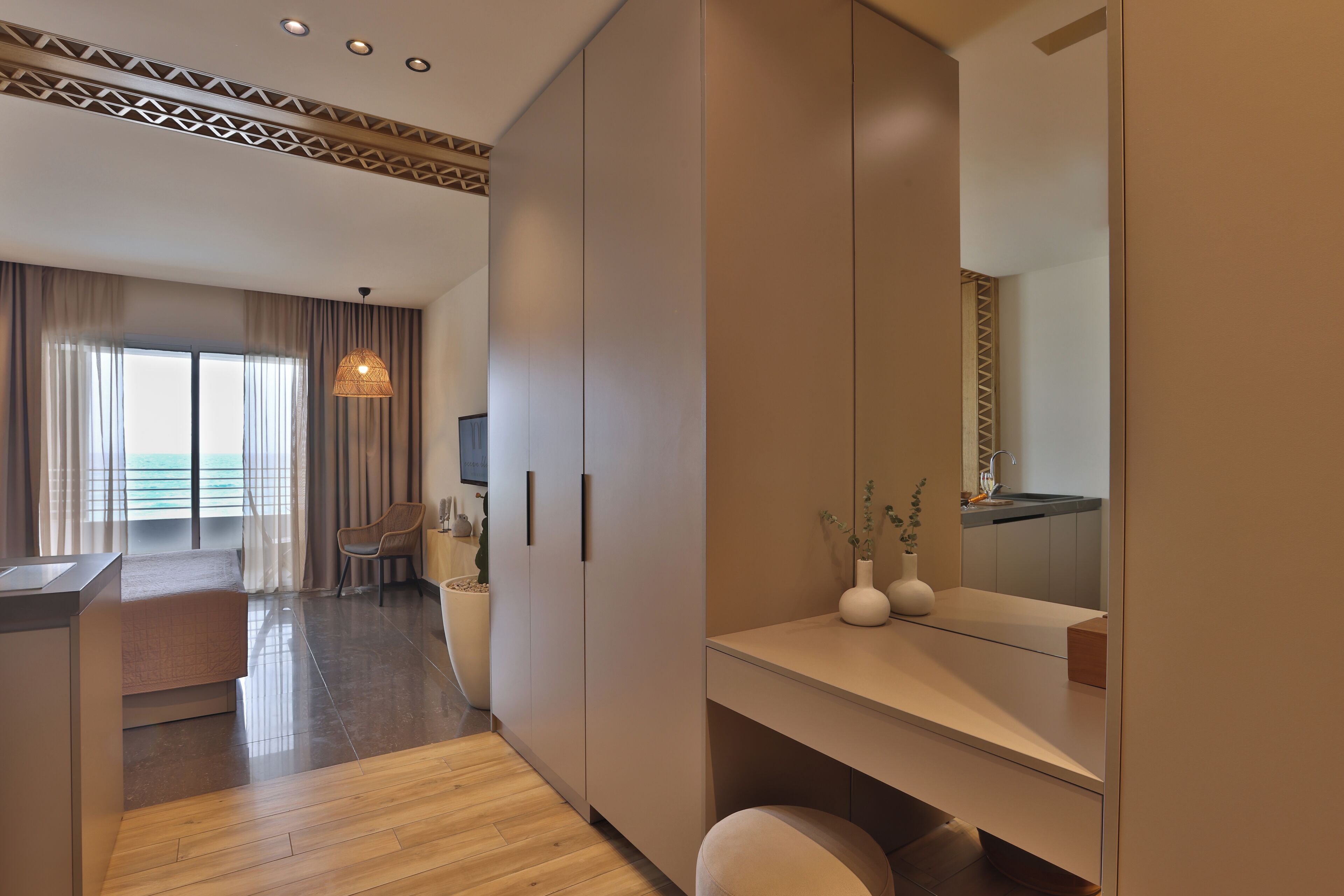 A modern hotel room with a large wardrobe, a dining area, and a view of the sea.