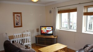 Un salon avec une télévision, une table en bois, un canapé en cuir noir et un berceau blanc.