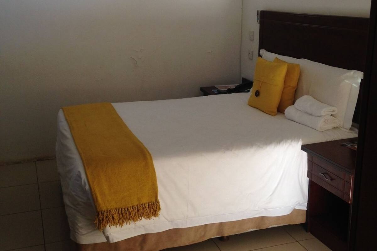 Una cama bien hecha con cubrecama blanco y marrón, una manta amarilla y dos almohadas.