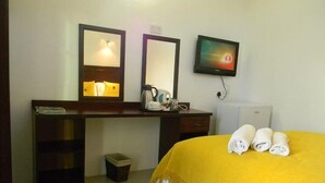 A hotel room with a bed, a desk with a mirror, a television, and a coffee maker. - White Palace Hotel (Serowe)