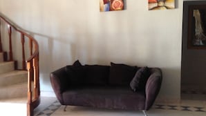 A living room with a dark-colored sofa, a staircase, and two pieces of wall art. - White Palace Hotel (Serowe)