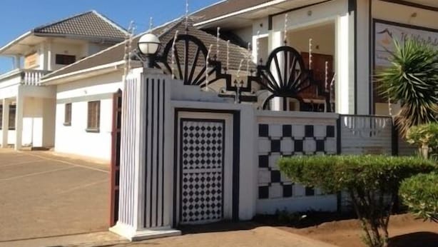 A modern two-story house with a gated entrance, a covered porch, and a paved driveway. - White Palace Hotel (Serowe)