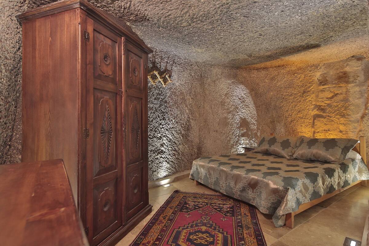 A bedroom with a wooden wardrobe, a bed with patterned bedding, and a decorative rug.