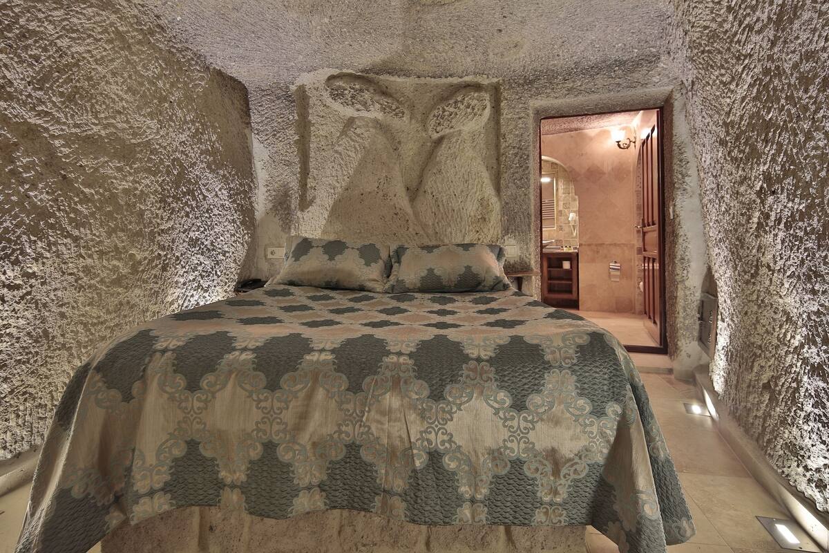 A bedroom with a large bed, a stone wall, and a wooden door leading to another room.