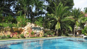A swimming pool with clear blue water, surrounded by lush greenery and a rocky artificial landscape. - Bohol Divers Resort (Tagbilaran)