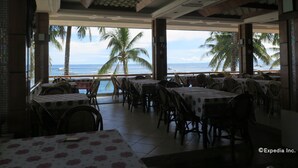 An indoor dining area with tables and chairs, a view of the ocean, and palm trees. - Bohol Divers Resort (Tagbilaran)